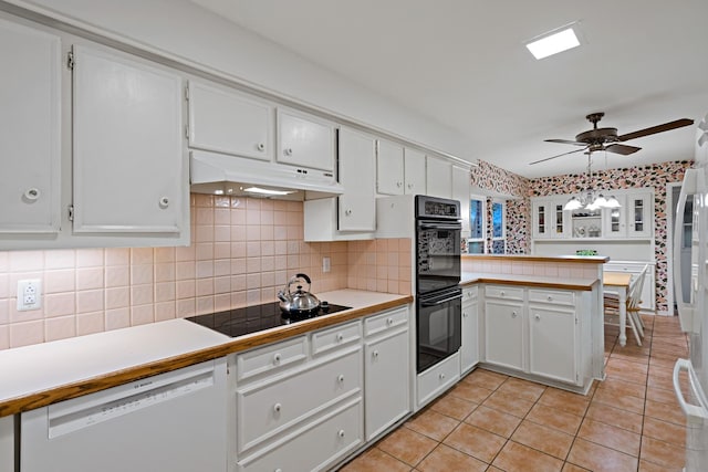 kitchen featuring white cabinets, light tile patterned flooring, a peninsula, under cabinet range hood, and black appliances