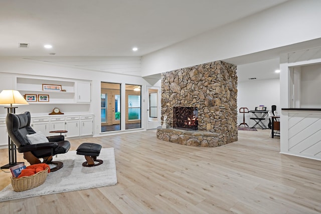 living area with light wood finished floors, a stone fireplace, recessed lighting, lofted ceiling, and visible vents