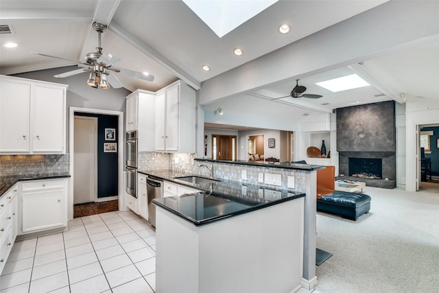 kitchen featuring a ceiling fan, a sink, a peninsula, and vaulted ceiling with skylight