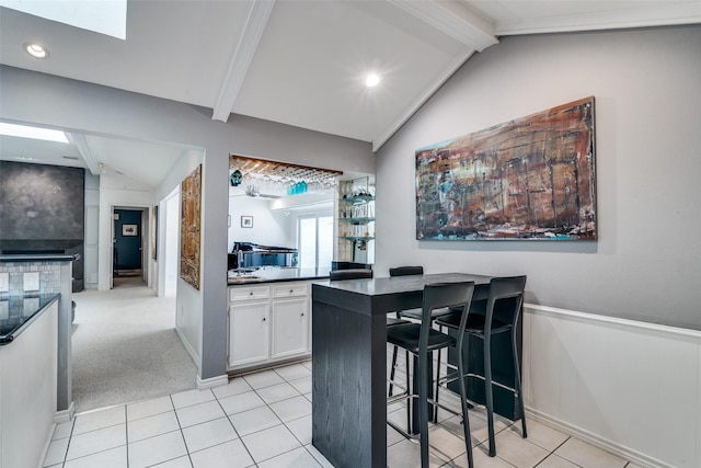 kitchen featuring wainscoting, dark countertops, a kitchen bar, white cabinets, and lofted ceiling with beams