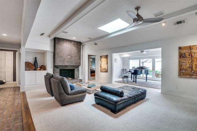 carpeted living area featuring a large fireplace, a ceiling fan, baseboards, a skylight, and visible vents