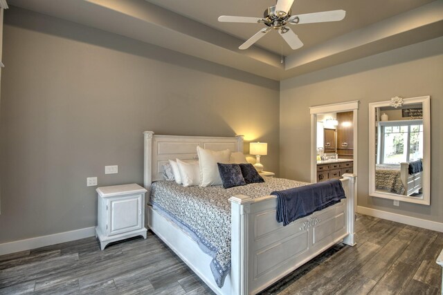 bedroom featuring dark wood-type flooring, baseboards, a raised ceiling, ensuite bathroom, and a ceiling fan