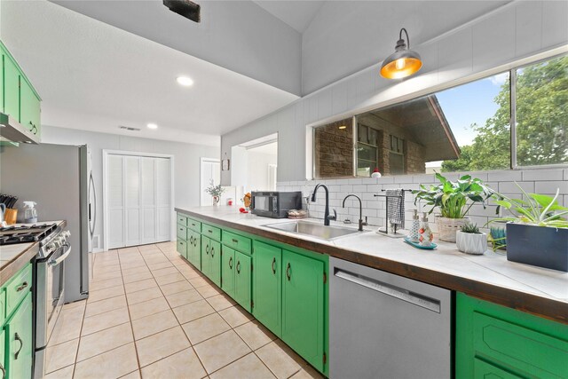 kitchen featuring green cabinetry, appliances with stainless steel finishes, a sink, decorative backsplash, and light tile patterned floors