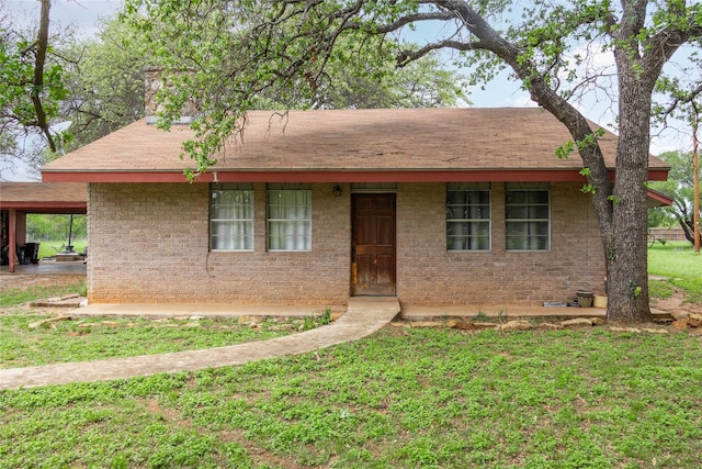 ranch-style house featuring brick siding, a shingled roof, a front lawn, and a chimney
