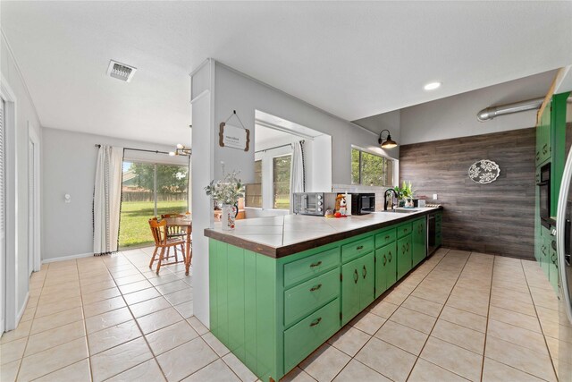 kitchen featuring tile counters, a sink, green cabinetry, and light tile patterned floors