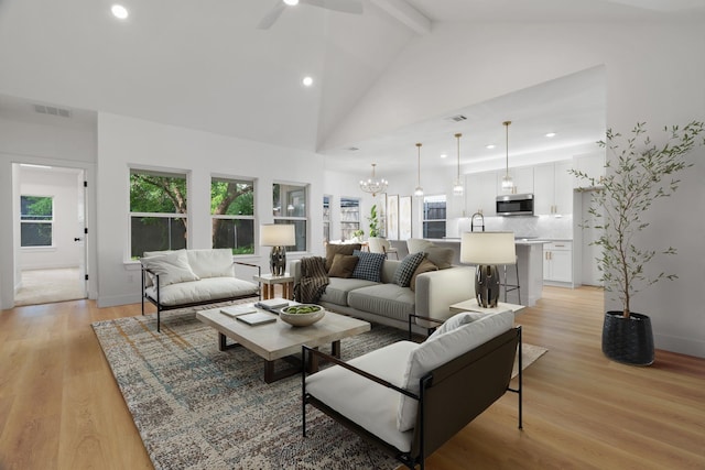 living room featuring light wood-style floors, beamed ceiling, ceiling fan with notable chandelier, and visible vents