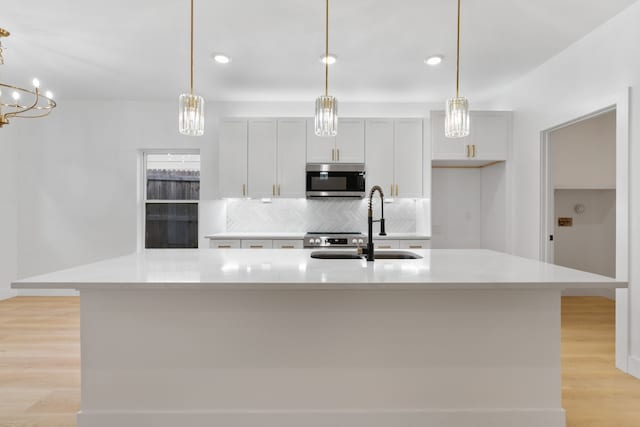 kitchen with light countertops, tasteful backsplash, stainless steel microwave, and light wood-type flooring
