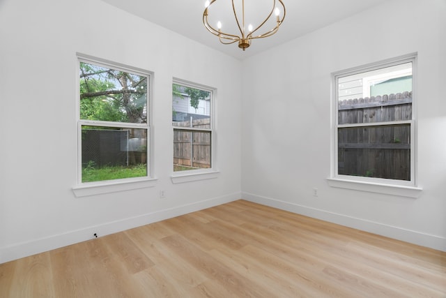 unfurnished room with baseboards, wood finished floors, and a notable chandelier