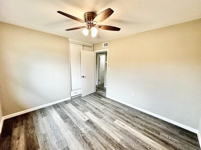 unfurnished bedroom with visible vents, a closet, wood finished floors, baseboards, and a ceiling fan