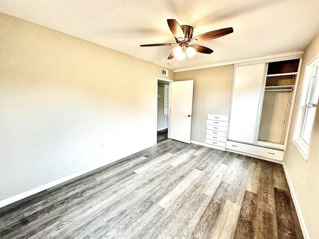 unfurnished bedroom with baseboards, a closet, wood finished floors, and visible vents