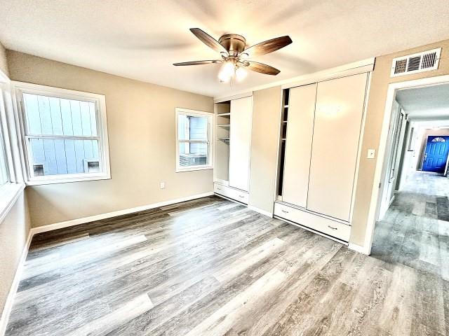 unfurnished bedroom with visible vents, multiple closets, wood finished floors, baseboards, and a ceiling fan