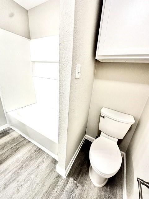 bathroom featuring baseboards, wood finished floors, and toilet