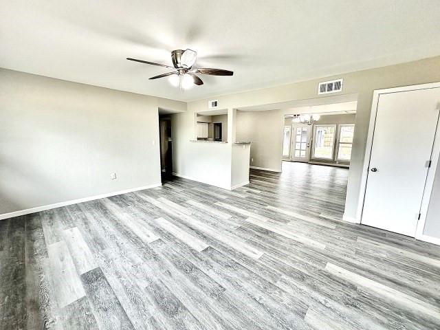 unfurnished living room featuring visible vents, baseboards, ceiling fan with notable chandelier, and wood finished floors