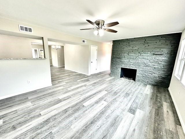 unfurnished living room with visible vents, wood finished floors, baseboards, a stone fireplace, and ceiling fan