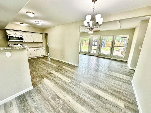 unfurnished dining area featuring baseboards, a notable chandelier, and wood finished floors