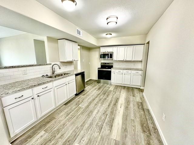 kitchen with appliances with stainless steel finishes, a sink, light wood finished floors, decorative backsplash, and visible vents