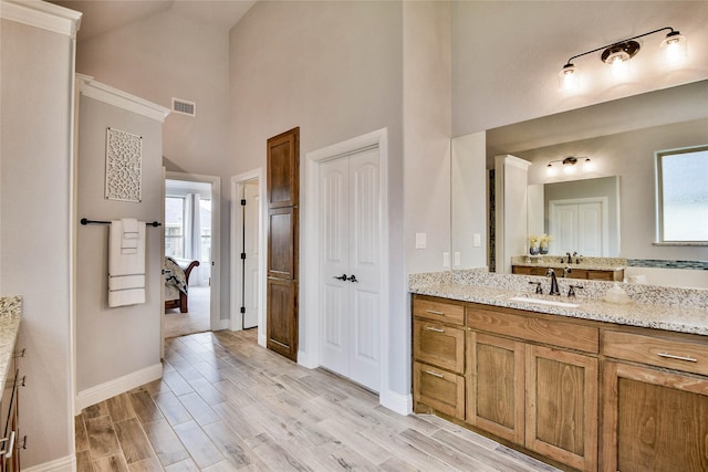 bathroom featuring connected bathroom, vanity, baseboards, a towering ceiling, and visible vents