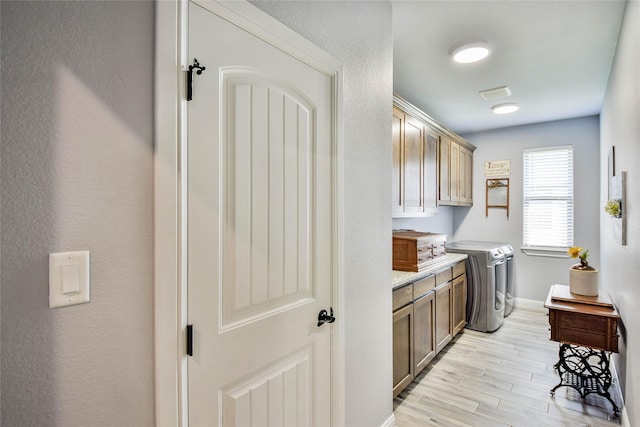 laundry area with light wood-type flooring, washer and clothes dryer, cabinet space, and baseboards
