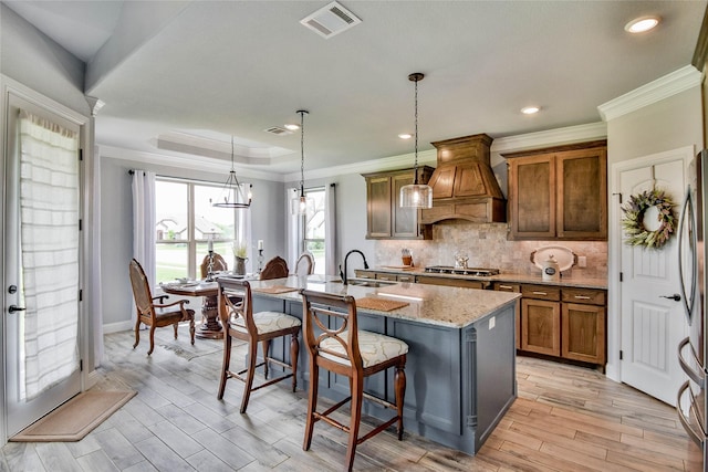 kitchen with visible vents, appliances with stainless steel finishes, brown cabinets, a sink, and custom range hood