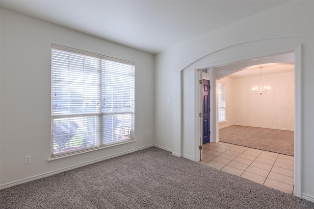 carpeted spare room featuring plenty of natural light, arched walkways, tile patterned floors, and an inviting chandelier