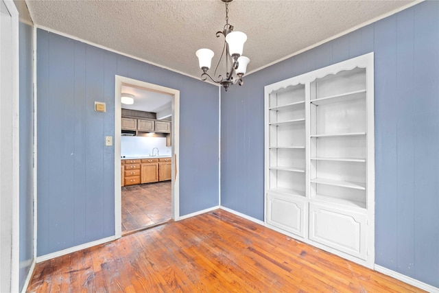 unfurnished dining area with an inviting chandelier, baseboards, hardwood / wood-style flooring, and a sink