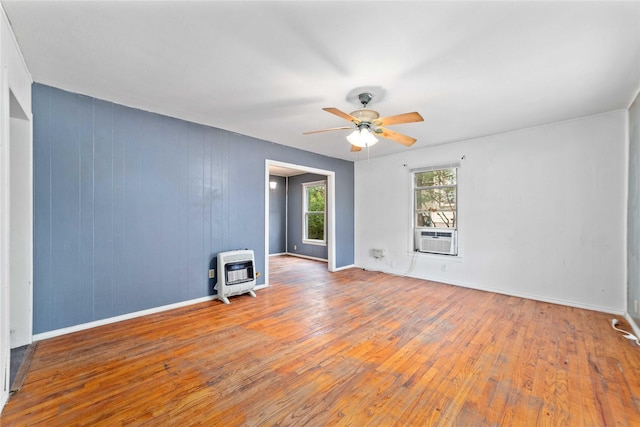 empty room with a wood stove, heating unit, hardwood / wood-style floors, baseboards, and ceiling fan