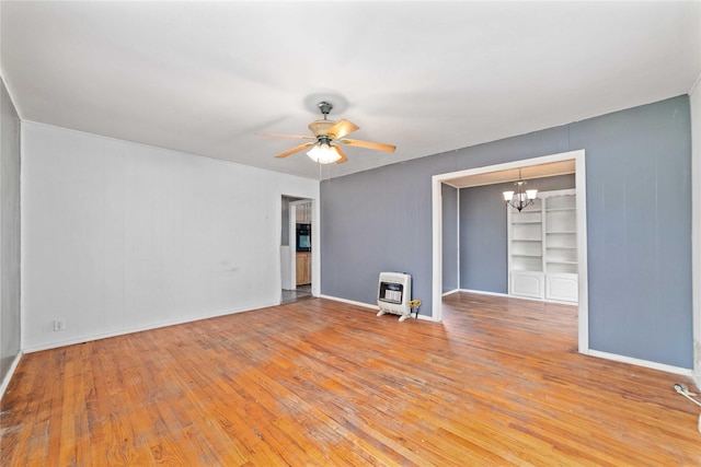 empty room featuring heating unit, a wood stove, light wood-type flooring, and ceiling fan with notable chandelier