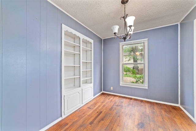 spare room with baseboards, a textured ceiling, wood finished floors, and a notable chandelier