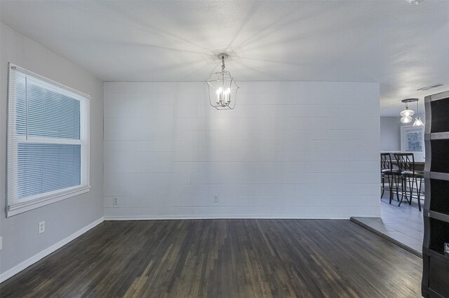 unfurnished dining area featuring an inviting chandelier, baseboards, and dark wood-style floors