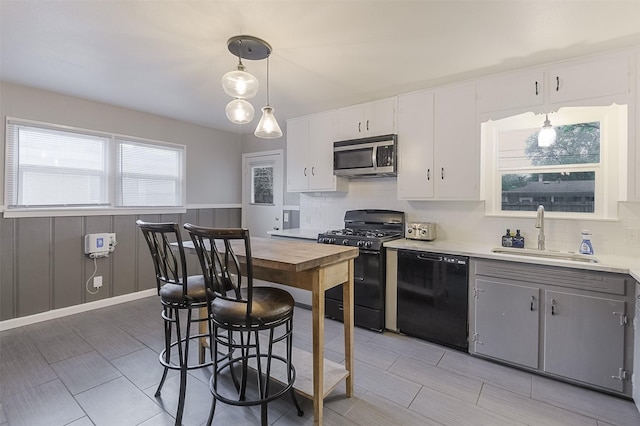 kitchen with a sink, light countertops, decorative backsplash, pendant lighting, and black appliances
