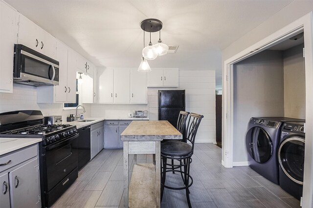 kitchen with a sink, black appliances, dark wood-style floors, and washer and dryer