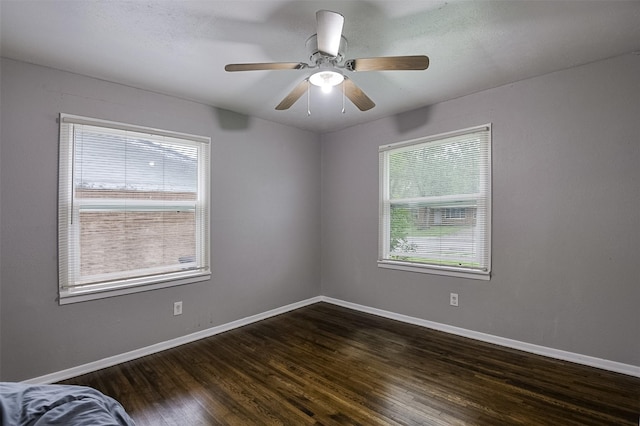 unfurnished room featuring baseboards, a ceiling fan, and dark wood finished floors