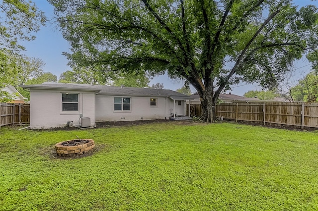 back of house featuring a fenced backyard, a lawn, a fire pit, and brick siding