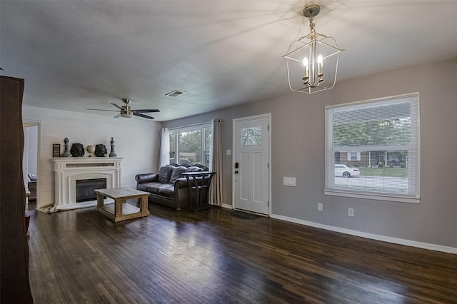 living room with a fireplace with raised hearth, ceiling fan with notable chandelier, baseboards, wood finished floors, and visible vents