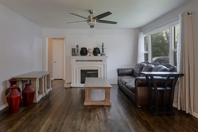 living room with a ceiling fan, baseboards, a fireplace with raised hearth, and dark wood-type flooring
