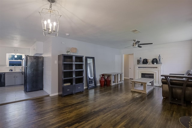 living room featuring a glass covered fireplace, ceiling fan with notable chandelier, dark wood-style flooring, and visible vents