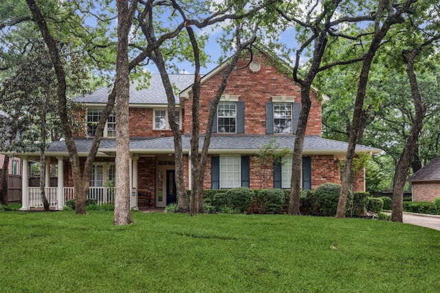 view of front of property featuring brick siding, a front lawn, and roof with shingles