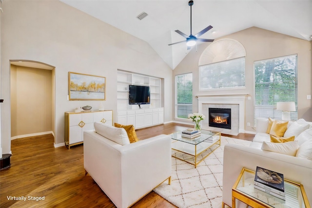 living area featuring a fireplace, built in shelves, a ceiling fan, baseboards, and wood finished floors