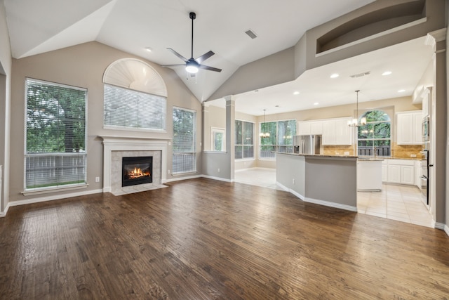 unfurnished living room with visible vents, ceiling fan with notable chandelier, light wood-style flooring, and lofted ceiling
