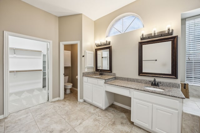 bathroom with double vanity, toilet, a walk in closet, and a sink