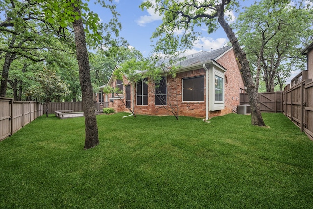 rear view of house featuring a yard, central AC unit, and a fenced backyard