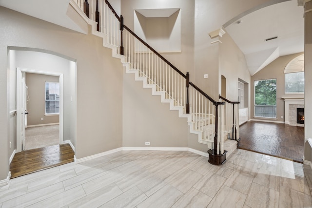 foyer entrance with arched walkways, high vaulted ceiling, stairs, baseboards, and wood finished floors