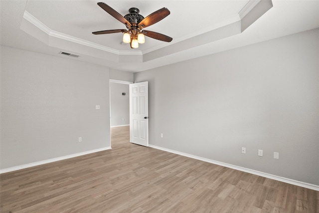unfurnished room with visible vents, a raised ceiling, crown molding, and light wood-style floors