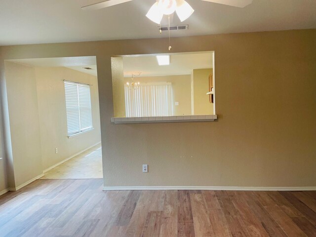spare room with baseboards, ceiling fan with notable chandelier, wood finished floors, and visible vents