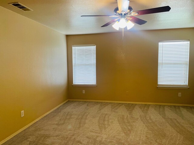 carpeted spare room with visible vents, a ceiling fan, a textured ceiling, and baseboards