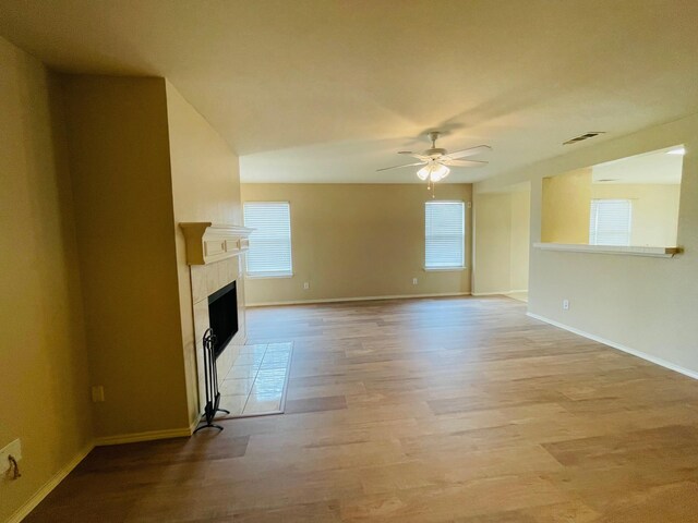 unfurnished living room with light wood-style floors, a ceiling fan, baseboards, and a tile fireplace