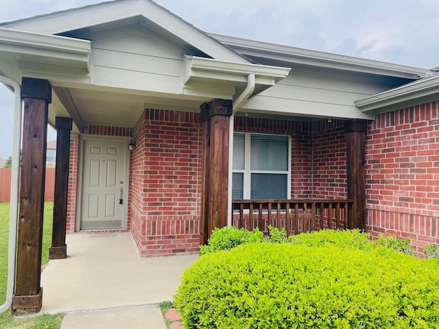view of exterior entry featuring a porch and brick siding