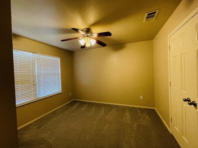 unfurnished room with dark carpet, baseboards, ceiling fan, and visible vents