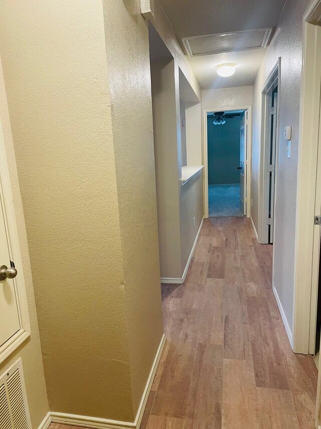 hall with baseboards, visible vents, a textured wall, and wood finished floors