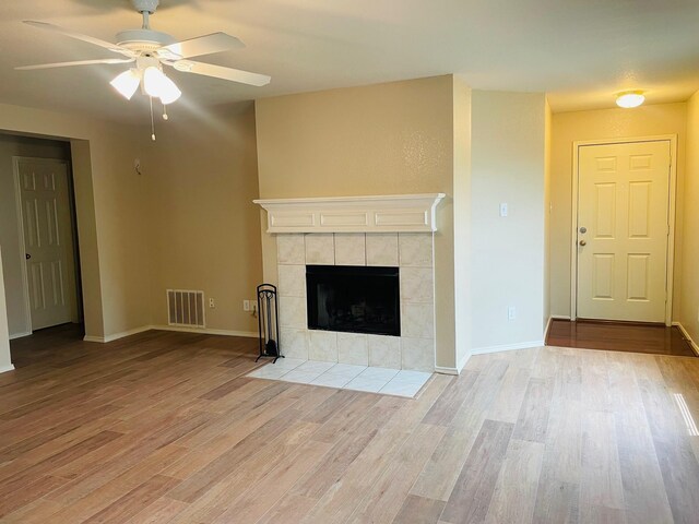 unfurnished living room with a ceiling fan, visible vents, wood finished floors, and a fireplace